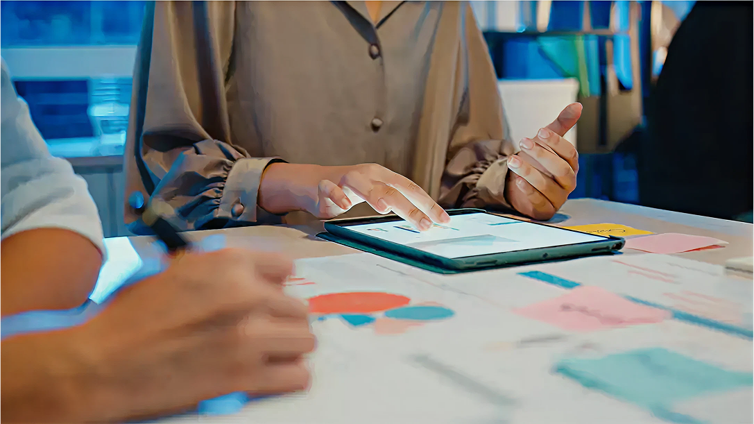 Persona utilizando una tablet táctil sobre una mesa con gráficos y notas adhesivas durante una reunión de trabajo