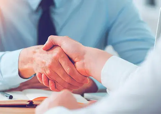 Primer plano de dos personas dándose la mano en señal de acuerdo, con fondo de oficina y vaso de agua.